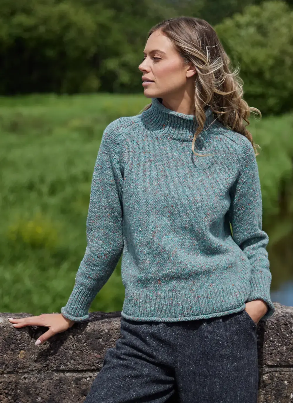Woman wearing a sea foam Donegal fleck saddle shoulder sweater by Fisherman Out of Ireland, made from mulesing-free merino wool